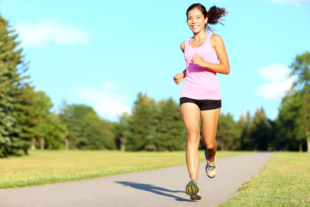 Sport fitness woman running in park on summer day. Asian female runner during outdoor workout. Fit sport fitness model of mixed Asian / Caucasian ethnicity.
